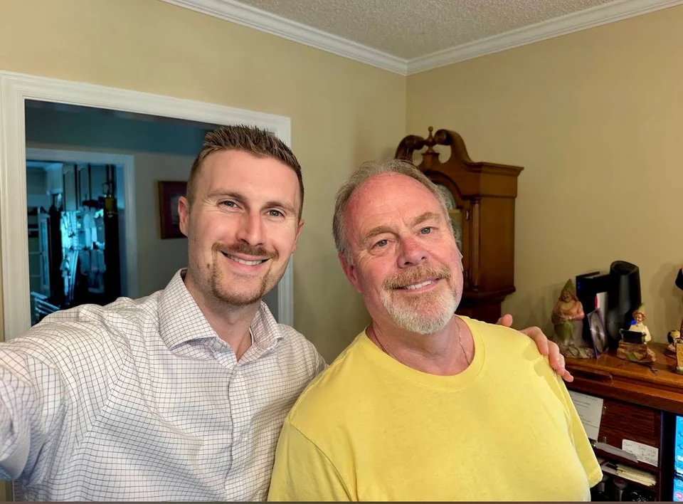 Preston beside a smiling man in a yellow shirt at home